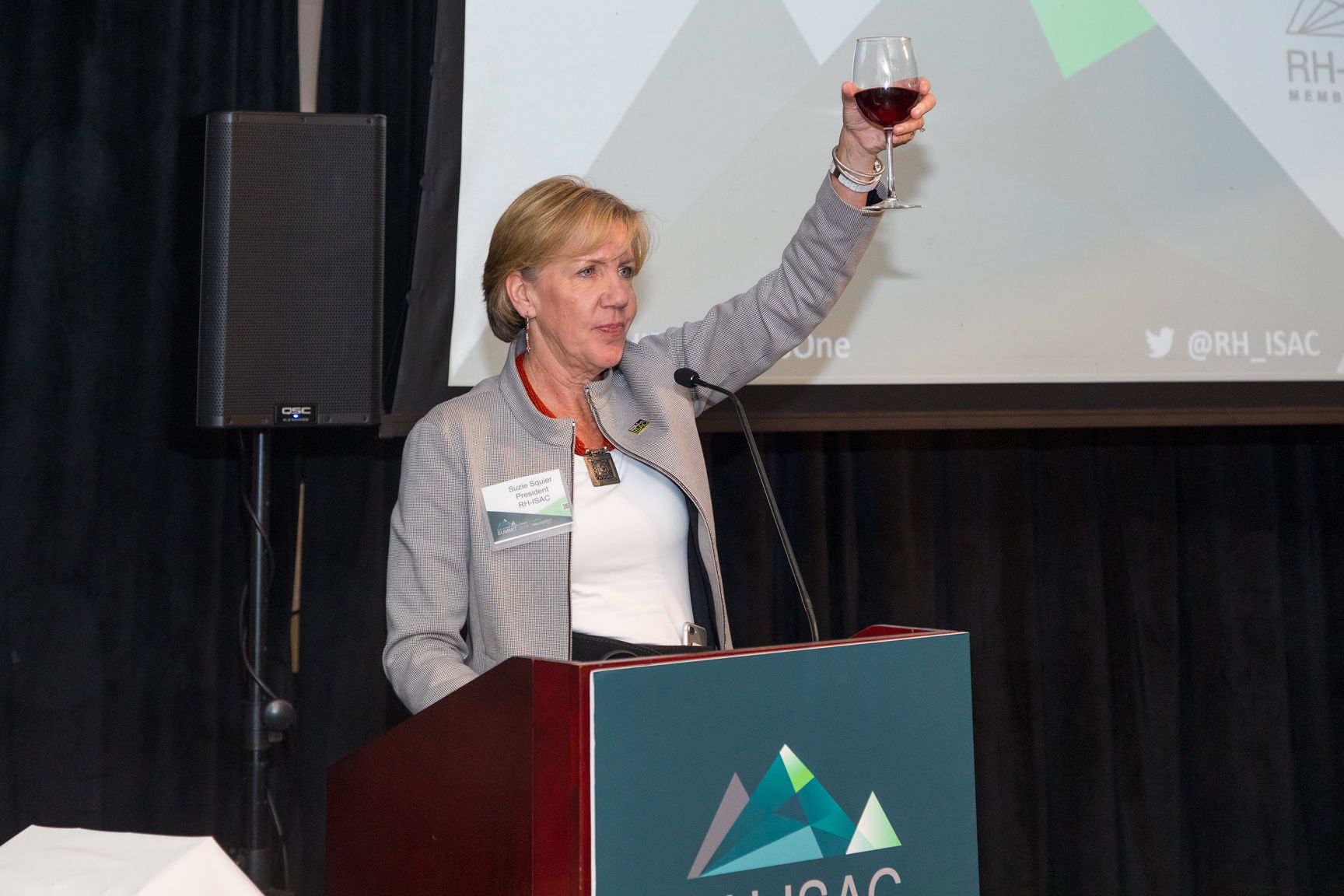 A women in a grey jacket lifts a glass of wine at a podium